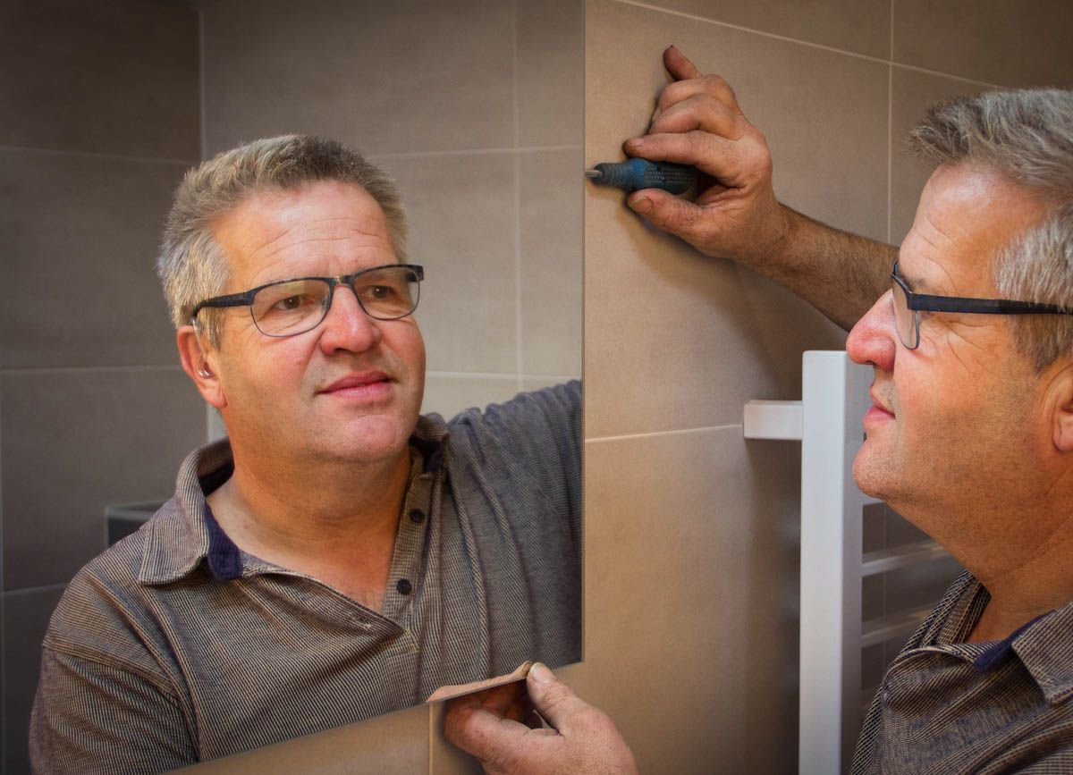 Peter Zegers monteert een spiegel in een badkamer